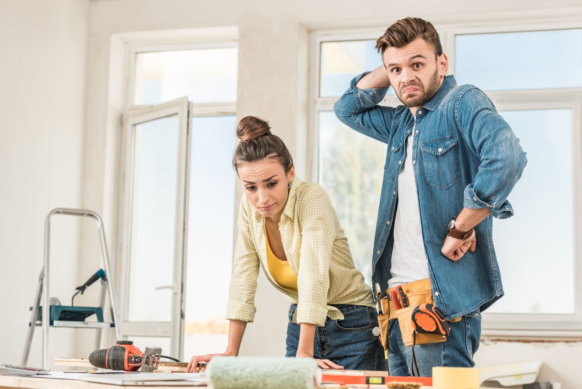 uncertain young couple standing near table with tools during repairment