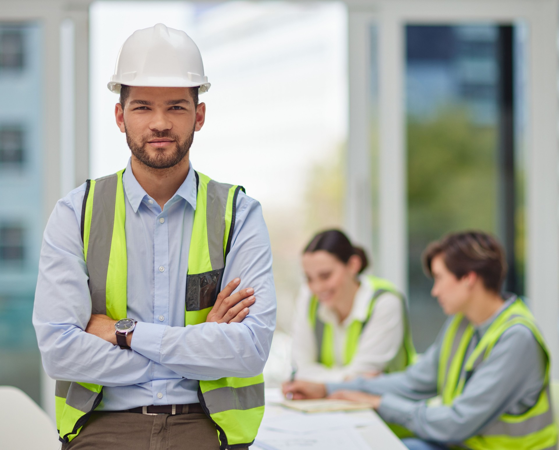 Cropped portrait of a handsome young male construction worker standing with his arms folded with his colleagues in the background